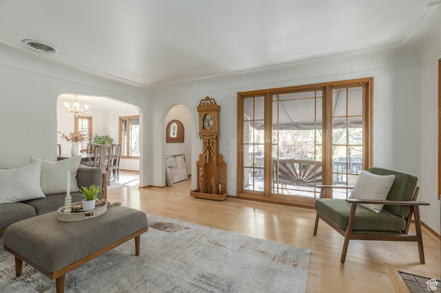living area with crown molding, arched walkways, light wood finished floors, a notable chandelier, and visible vents