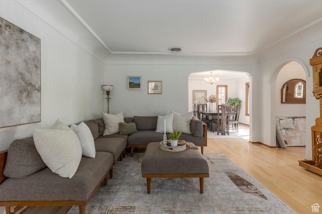 living room with arched walkways, visible vents, an inviting chandelier, wood finished floors, and crown molding