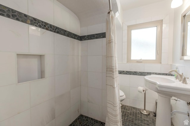 full bath with a tile shower, tile walls, and toilet