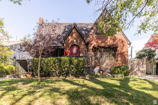tudor house featuring fence, a front lawn, and brick siding
