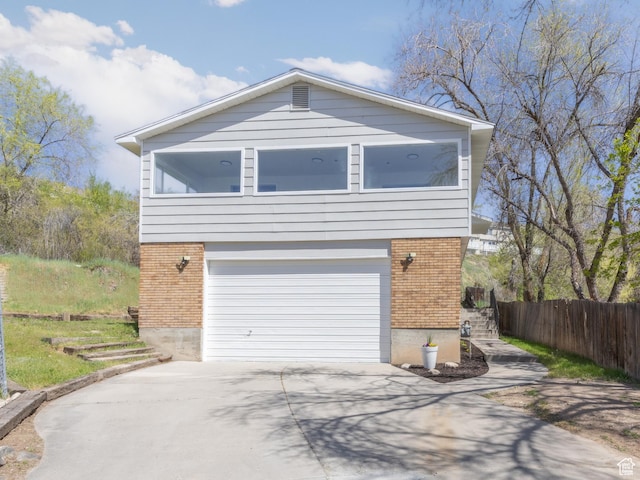 view of front of property featuring an attached garage, brick siding, fence, and driveway