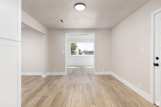 unfurnished room featuring a textured ceiling, light wood-type flooring, visible vents, and baseboards