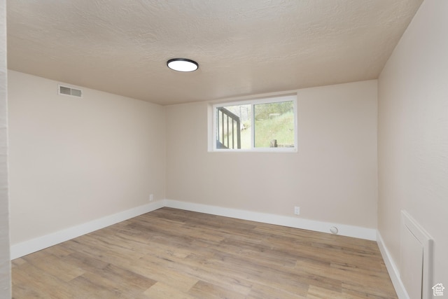 empty room with light wood-type flooring, baseboards, visible vents, and a textured ceiling