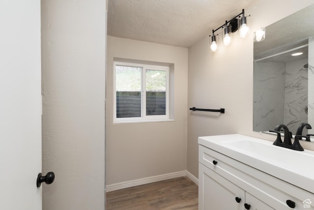 full bathroom featuring a textured ceiling, baseboards, walk in shower, wood finished floors, and vanity