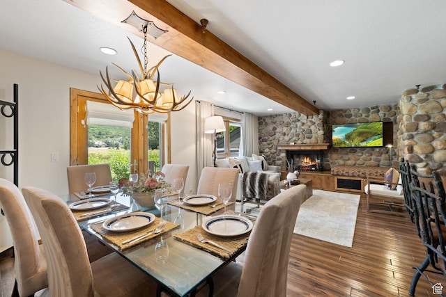 dining space with wood finished floors, a stone fireplace, an inviting chandelier, beam ceiling, and recessed lighting