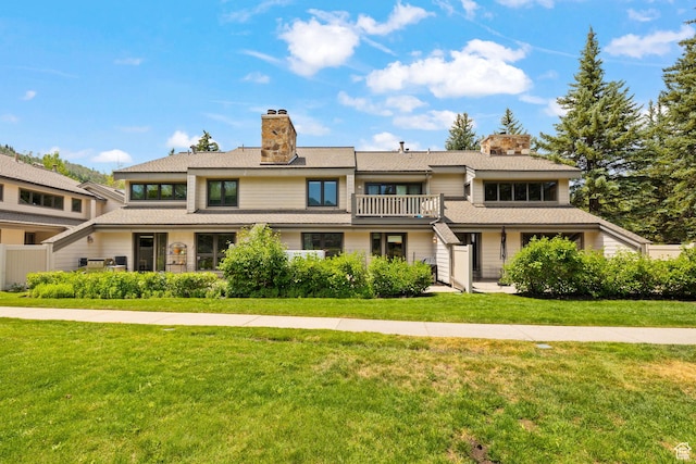 view of front of home featuring a front yard, a chimney, and a balcony