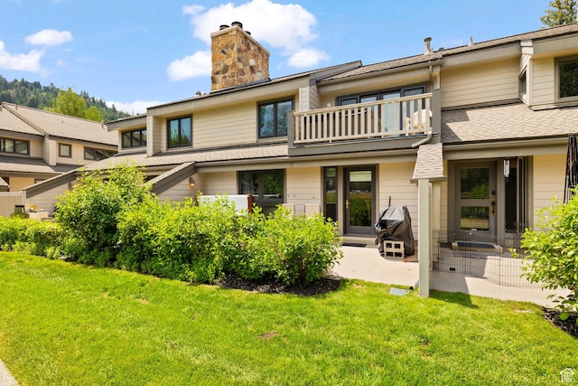 rear view of house featuring a chimney, a patio, a yard, and a balcony