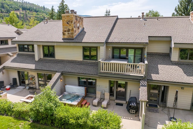 back of property with a shingled roof, a patio, a balcony, and a chimney