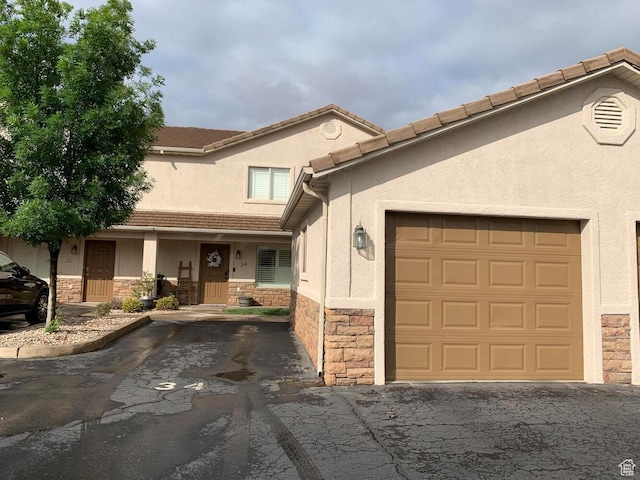 view of front of house featuring stone siding, aphalt driveway, a garage, and stucco siding