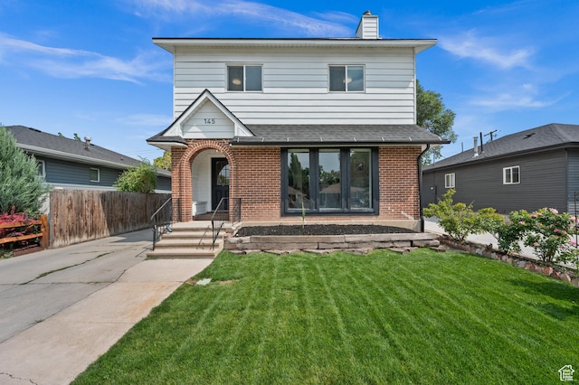 traditional home with a front lawn, a chimney, covered porch, fence, and brick siding