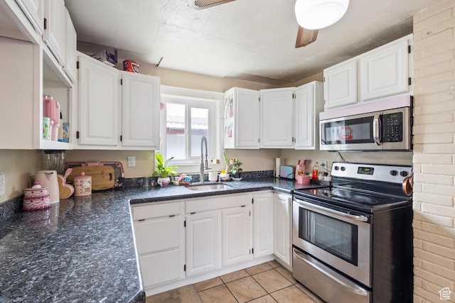 kitchen featuring dark stone countertops, a sink, light tile patterned floors, stainless steel appliances, and white cabinetry