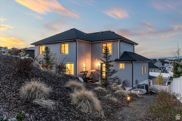 back of house at dusk with a shingled roof and fence