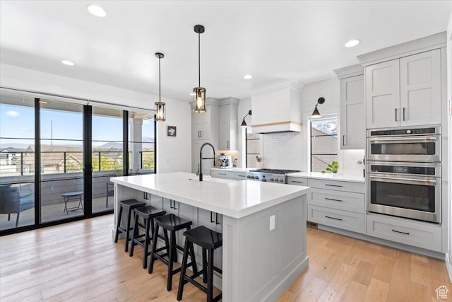 kitchen with a center island with sink, light wood-style floors, a kitchen bar, backsplash, and light countertops