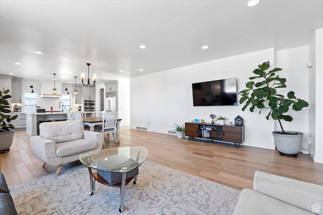 living room with light wood finished floors, baseboards, an inviting chandelier, recessed lighting, and visible vents