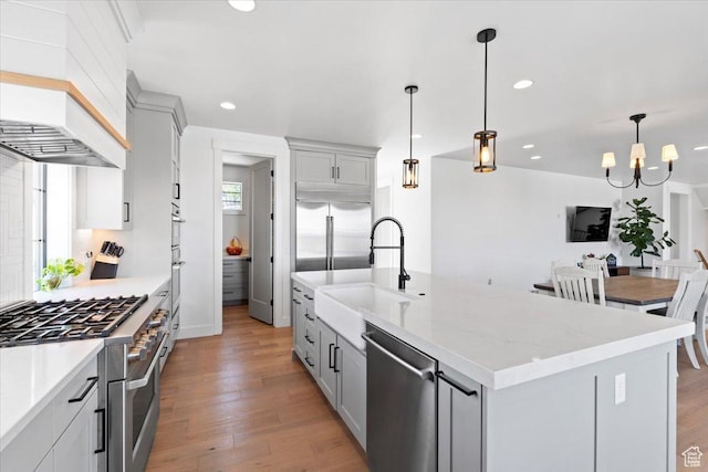 kitchen featuring recessed lighting, an island with sink, light wood-style floors, high quality appliances, and custom range hood