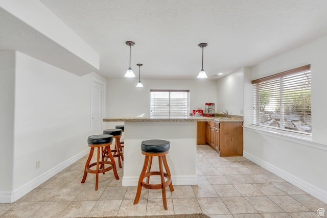 kitchen with brown cabinets, a breakfast bar, light tile patterned floors, decorative light fixtures, and baseboards
