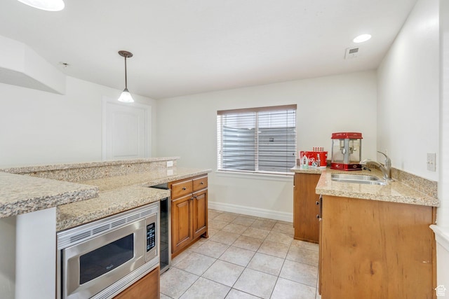 kitchen featuring brown cabinets, visible vents, light tile patterned floors, stainless steel microwave, and a sink