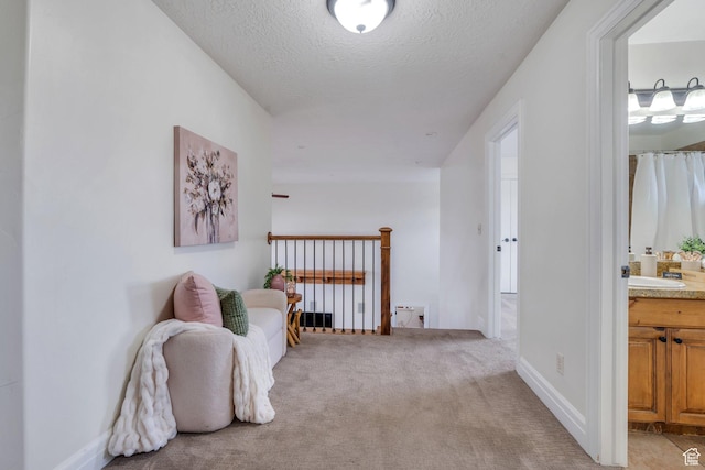 corridor with baseboards, a textured ceiling, and light colored carpet
