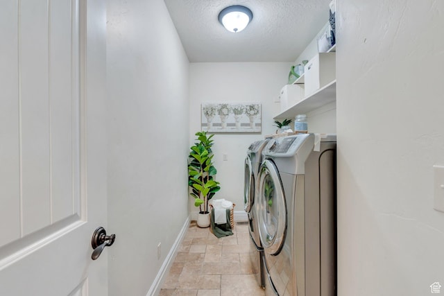 clothes washing area with laundry area, stone finish flooring, washing machine and clothes dryer, baseboards, and a textured ceiling