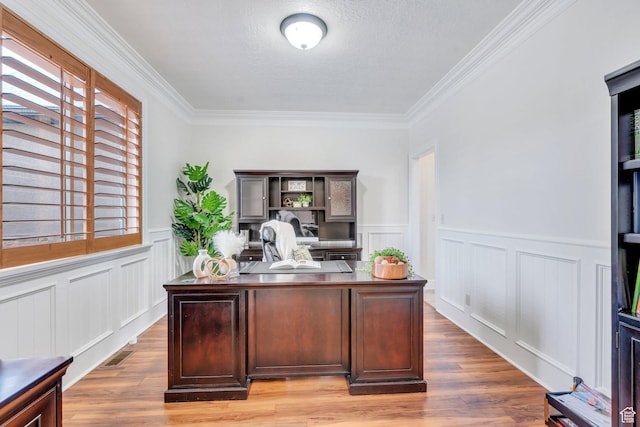 office area featuring light wood-type flooring, a decorative wall, crown molding, and wainscoting