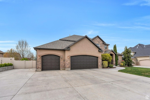 french country inspired facade with stone siding, concrete driveway, fence, an attached garage, and stucco siding