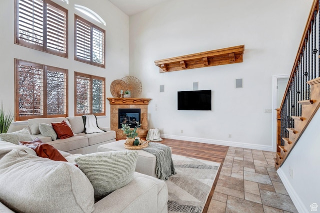 living room featuring stone tile floors, baseboards, a towering ceiling, stairway, and a fireplace