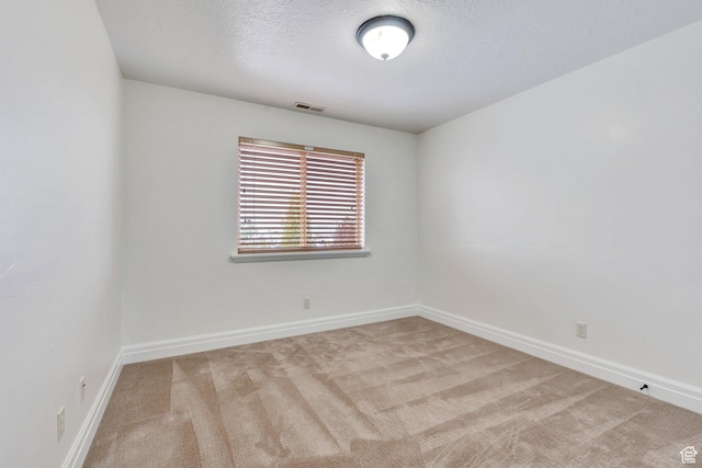 spare room featuring carpet floors, a textured ceiling, visible vents, and baseboards