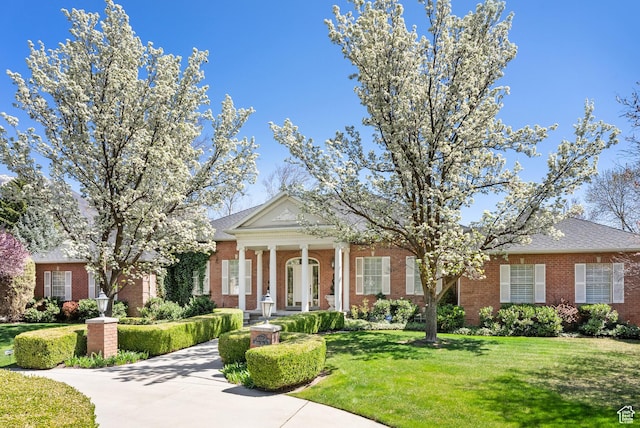 neoclassical / greek revival house featuring brick siding and a front yard