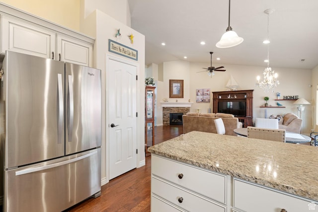 kitchen with dark wood finished floors, vaulted ceiling, freestanding refrigerator, ceiling fan with notable chandelier, and a fireplace