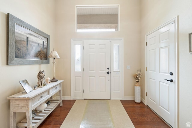 foyer entrance featuring a towering ceiling, baseboards, and dark wood-style flooring