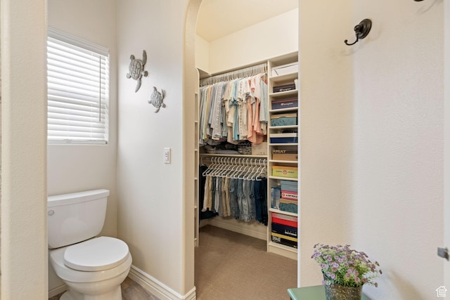bathroom featuring a walk in closet, toilet, and baseboards