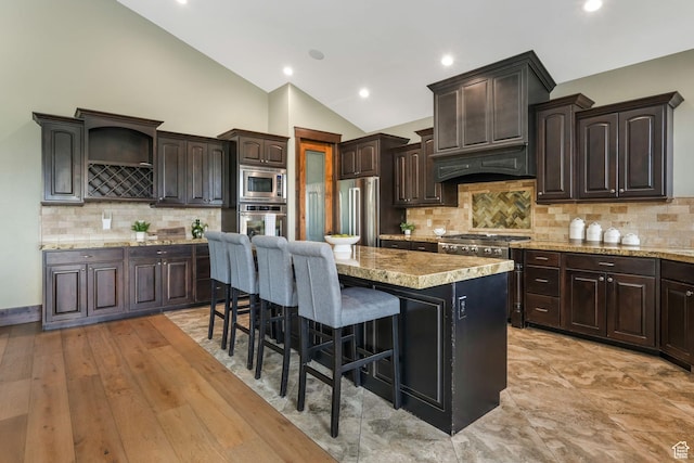 kitchen featuring stainless steel appliances, a center island, vaulted ceiling, dark brown cabinetry, and a breakfast bar area
