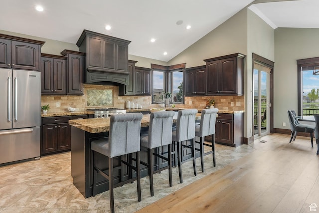 kitchen featuring a kitchen breakfast bar, dark brown cabinets, high end fridge, backsplash, and a kitchen island
