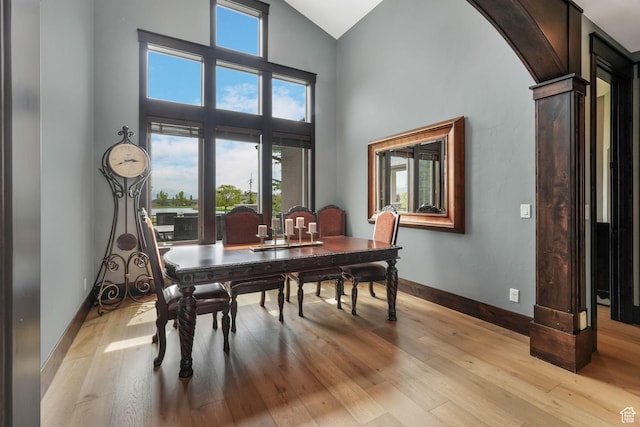 dining room featuring high vaulted ceiling, arched walkways, light wood-style floors, and baseboards
