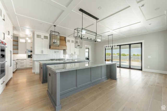 3640 W Kenna Ln Unit 101, Bluffdale, UT 84065 - kitchen featuring decorative backsplash, a large island with sink, light wood finished floors, white cabinets, and coffered ceiling