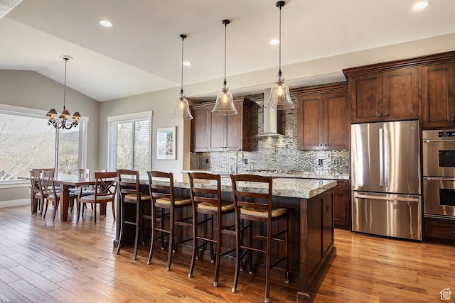 1621 S 4800 E, Heber City, UT 84032 - kitchen with appliances with stainless steel finishes, wall chimney exhaust hood, light wood-style floors, a center island with sink, and vaulted ceiling