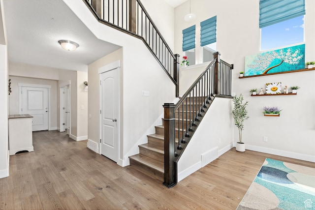 stairs with baseboards, a towering ceiling, wood finished floors, and visible vents