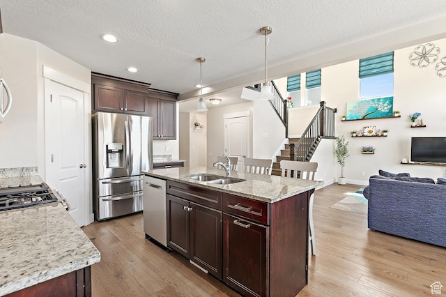 kitchen featuring a textured ceiling, a sink, open floor plan, stainless steel appliances, and light wood-style flooring