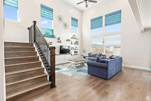 living room with stairway, a towering ceiling, ceiling fan, and wood-type flooring