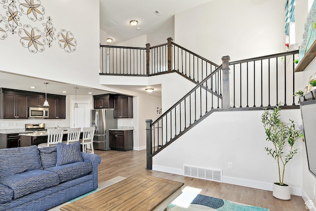 living area featuring a towering ceiling, baseboards, visible vents, light wood-style floors, and stairs