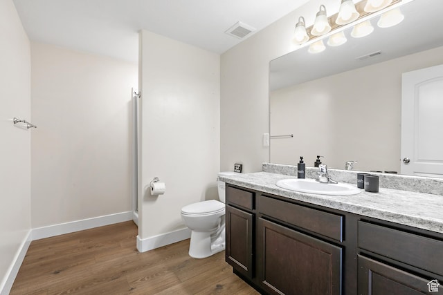 bathroom with toilet, vanity, wood finished floors, and visible vents