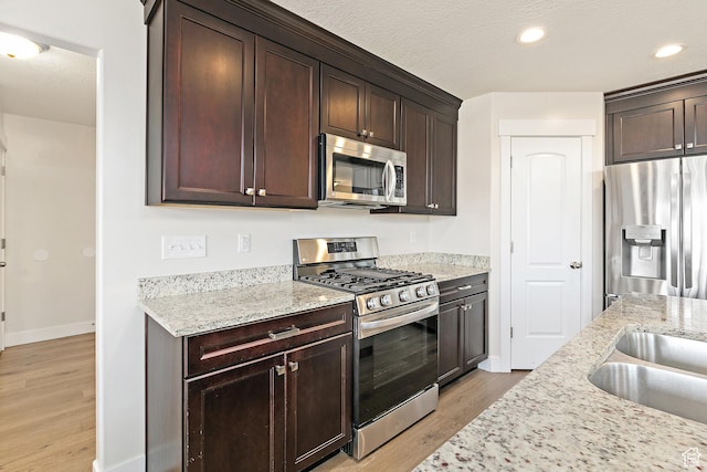 kitchen with stainless steel appliances, light wood-type flooring, baseboards, dark brown cabinetry, and light stone countertops