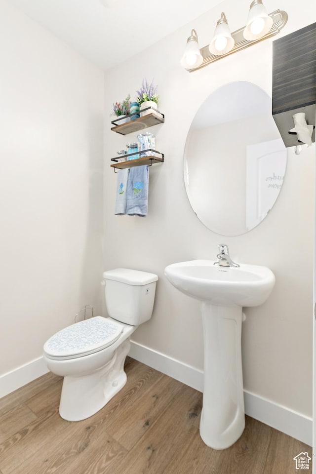 half bathroom with wood finished floors, baseboards, and toilet