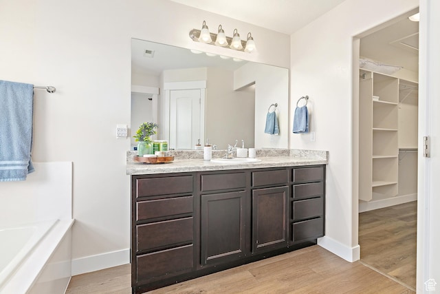 full bathroom with a walk in closet, baseboards, vanity, and wood finished floors