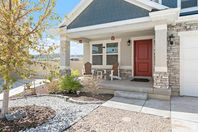 view of exterior entry featuring stucco siding, stone siding, covered porch, and fence
