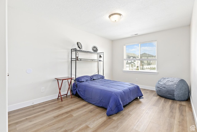bedroom featuring visible vents, baseboards, wood finished floors, and a textured ceiling