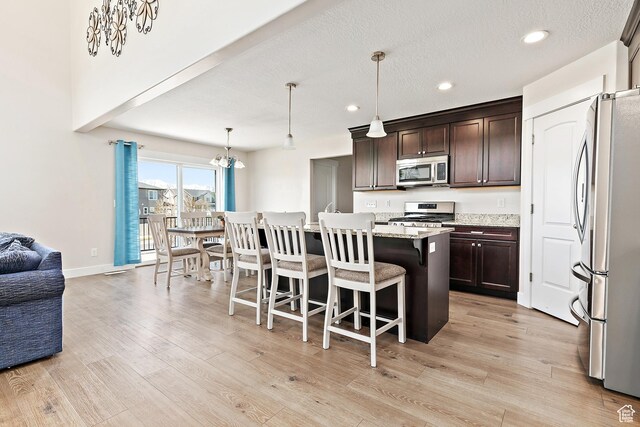 kitchen with a kitchen breakfast bar, dark brown cabinets, light wood-type flooring, appliances with stainless steel finishes, and open floor plan