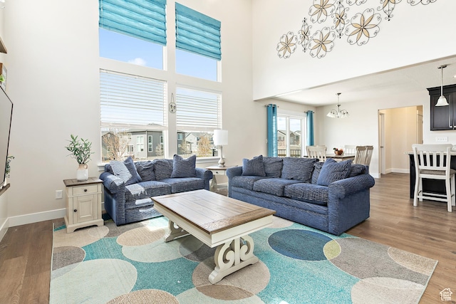 living room with a chandelier, wood finished floors, a towering ceiling, and baseboards