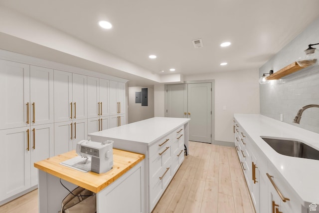kitchen with a center island, a sink, wooden counters, and white cabinetry