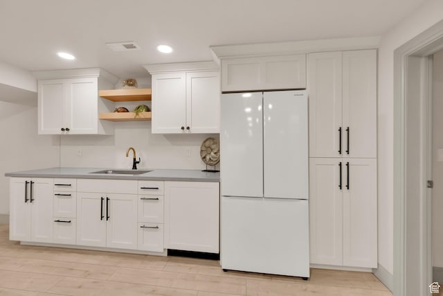 kitchen with open shelves, freestanding refrigerator, a sink, and white cabinetry